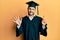 Young hispanic man wearing graduation cap and ceremony robe showing and pointing up with fingers number six while smiling