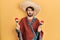 Young hispanic man wearing mexican hat holding maracas clueless and confused expression