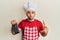 Young hispanic man wearing professional cook uniform holding grater and cheese looking at the camera blowing a kiss being lovely