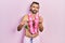 Young hispanic man wearing swimsuit and hawaiian lei drinking tropical cocktail doing money gesture with hands, asking for salary