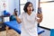 Young hispanic physiotherapist woman holding hand grip to train muscle doing video call afraid and shocked with surprise and