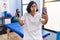 Young hispanic physiotherapist woman holding hand grip to train muscle doing video call puffing cheeks with funny face