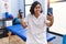 Young hispanic physiotherapist woman holding hand grip to train muscle doing video call sticking tongue out happy with funny