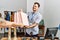 Young hispanic shopkeeper man smiling happy giving shopping bags to customer at clothing store