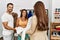 Young hispanic shopkeeper woman showing shirt to hispanic couple at clothes store