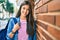 Young hispanic student girl smiling happy leaning on the wall at the city