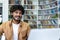 Young hispanic student studying inside university campus academic library among bookshelves, man smiling and using