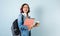 Young Hispanic student woman wearing backpack and holding books and tablet over isolated blue background