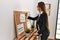 Young hispanic woman business worker writing on corkboard at office