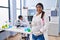 Young hispanic woman expecting a baby working at scientist laboratory looking positive and happy standing and smiling with a