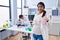 Young hispanic woman expecting a baby working at scientist laboratory smiling happy and positive, thumb up doing excellent and