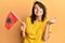 Young hispanic woman holding albania flag screaming proud, celebrating victory and success very excited with raised arm