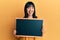 Young hispanic woman holding blackboard sticking tongue out happy with funny expression