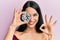 Young hispanic woman holding brilliant diamond stone on eye doing ok sign with fingers, smiling friendly gesturing excellent