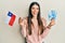 Young hispanic woman holding chile flag and chilean pesos banknotes smiling and laughing hard out loud because funny crazy joke