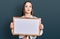 Young hispanic woman holding empty white chalkboard looking at the camera blowing a kiss being lovely and sexy