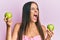 Young hispanic woman holding green apples angry and mad screaming frustrated and furious, shouting with anger