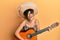 Young hispanic woman holding mexican hat playing classical guitar smiling and laughing hard out loud because funny crazy joke