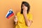 Young hispanic woman holding slovenia flag covering mouth with hand, shocked and afraid for mistake