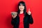 Young hispanic woman holding sunflower seeds bowl smiling with an idea or question pointing finger with happy face, number one