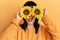 Young hispanic woman holding sunflowers over eyes angry and mad screaming frustrated and furious, shouting with anger looking up