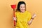 Young hispanic woman holding toilet plunger screaming proud, celebrating victory and success very excited with raised arm