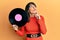 Young hispanic woman holding vinyl disc serious face thinking about question with hand on chin, thoughtful about confusing idea