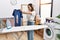 Young hispanic woman ironing holding burned iron shirt at laundry room clueless and confused expression