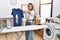 Young hispanic woman ironing holding burned iron shirt at laundry room sticking tongue out happy with funny expression