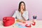 Young hispanic woman making valentine gift sitting on the table hand on mouth telling secret rumor, whispering malicious talk