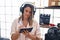 Young hispanic woman musician listening to music composing song at music studio