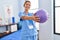 Young hispanic woman physiotherapist stretching arms using ball at rehab clinic