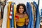 Young hispanic woman searching clothes on clothing rack using smartphone with a happy and cool smile on face