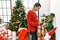 Young hispanic woman smiling confident looking picture standing by christmas tree at home