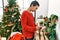 Young hispanic woman smiling confident looking picture standing by christmas tree at home