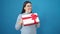 Young hispanic woman smiling holding gift over isolated blue background