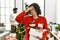 Young hispanic woman standing by christmas tree with decoration tired rubbing nose and eyes feeling fatigue and headache