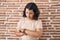 Young hispanic woman standing over bricks wall checking the time on wrist watch, relaxed and confident