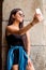 Young hispanic woman strolling around a square in the city while using her electronic devices