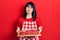 Young hispanic woman wearing cook apron holding board with meat looking at the camera blowing a kiss being lovely and sexy