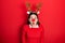 Young hispanic woman wearing deer christmas hat and red nose afraid and shocked with surprise and amazed expression, fear and