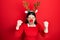 Young hispanic woman wearing deer christmas hat and red nose angry and mad raising fists frustrated and furious while shouting