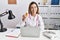 Young hispanic woman wearing doctor uniform holding pills at the clinic smiling looking to the side and staring away thinking