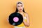 Young hispanic woman wearing pin up style holding vinyl disc relaxed with serious expression on face