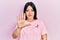 Young hispanic woman wearing pink cancer ribbon on t shirt doing stop sing with palm of the hand