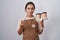 Young hispanic woman wearing professional waitress apron holding coffee doing money gesture with hands, asking for salary payment,