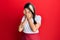 Young hispanic woman wearing professional waitress apron with sad expression covering face with hands while crying