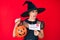 Young hispanic woman wearing witch costume holding pumpkin and happy halloween message angry and mad screaming frustrated and