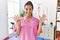 Young hispanic woman working at pain recovery clinic showing and pointing up with fingers number nine while smiling confident and