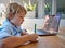 Young homeschool little boy sitting alone and using laptop to study. Caucasian child writing and learning remotely due